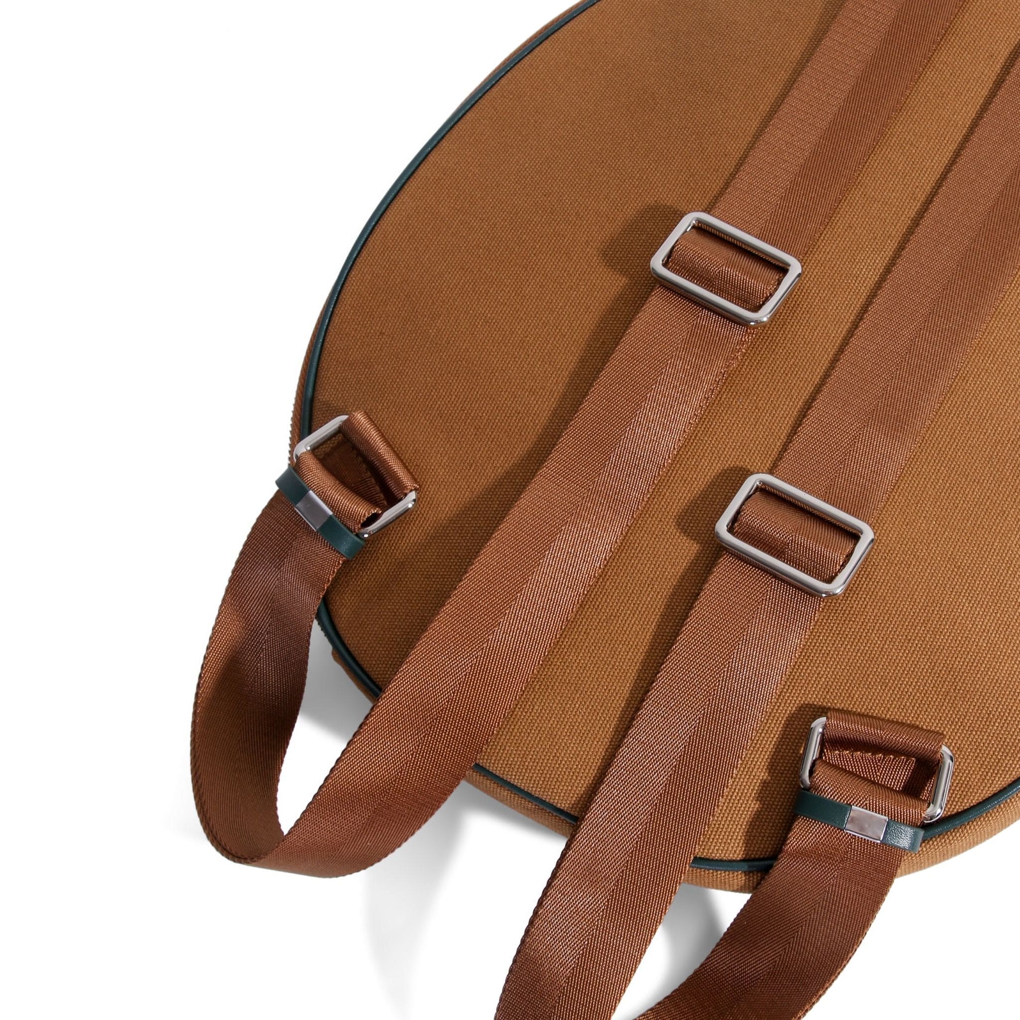 Close-up of the back of a brown canvas tennis bag showing two adjustable straps with silver metal buckles, set against a white background.