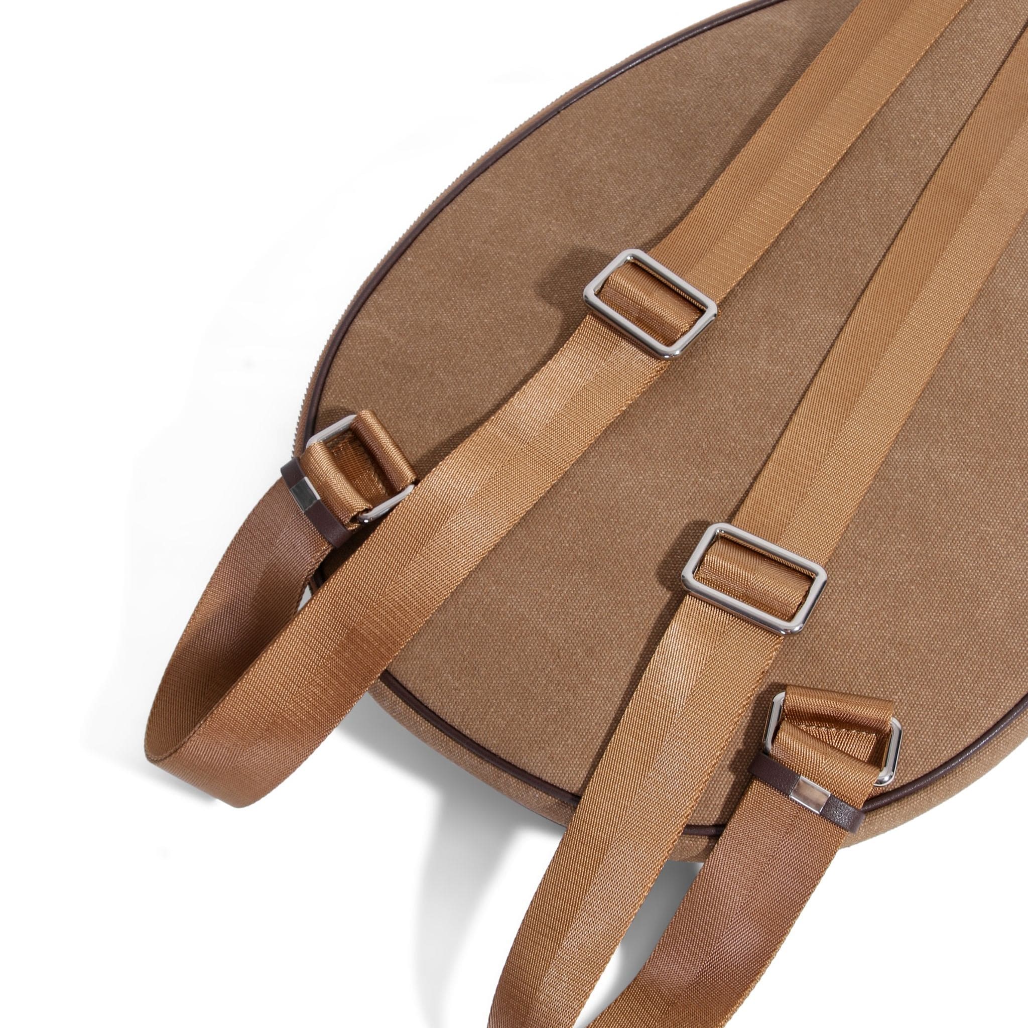 Close-up of a brown canvas tennis bag with tan adjustable shoulder straps, silver buckles, and a rounded top, set against a white background.