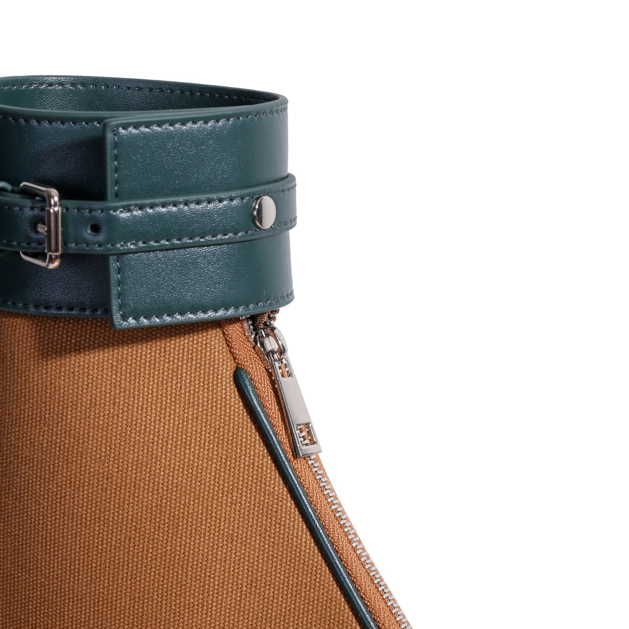 Close-up of a stylish boot, featuring brown textured fabric reminiscent of a canvas tennis bag, with a diagonal silver zipper and a dark green leather cuff with buckle and metal snap detail at the top.