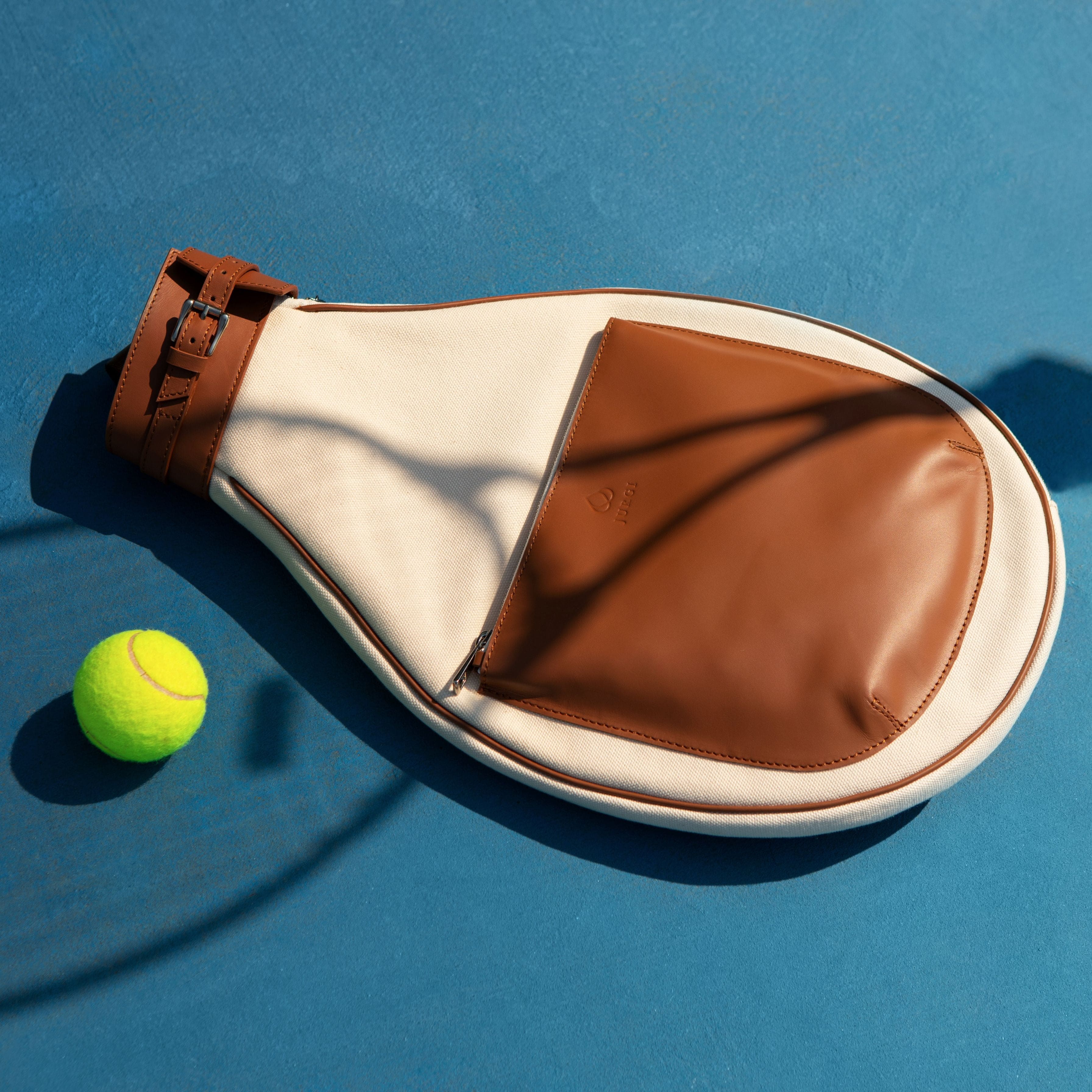 Tennis racket head cover with a tennis ball on a blue surface