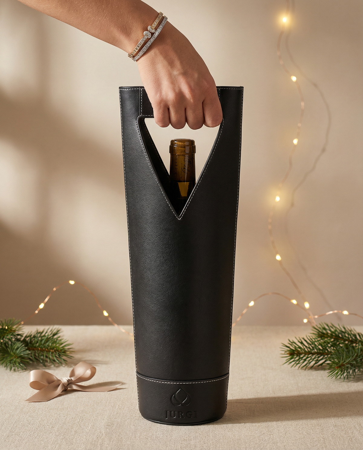 Black wine bottle holder with a bottle inside, held by a hand against a neutral background with string lights.