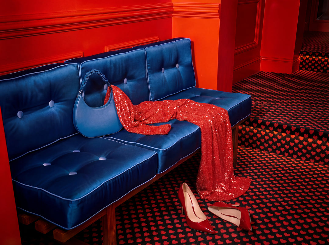 Blue tufted sofa with red sequin dress and high heels in a room with red walls and black and red checkered floor.