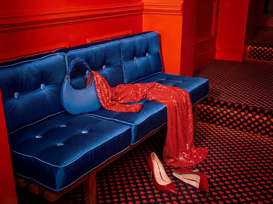 Blue tufted sofa with red sequin dress and high heels in a room with red walls and black and red checkered floor.