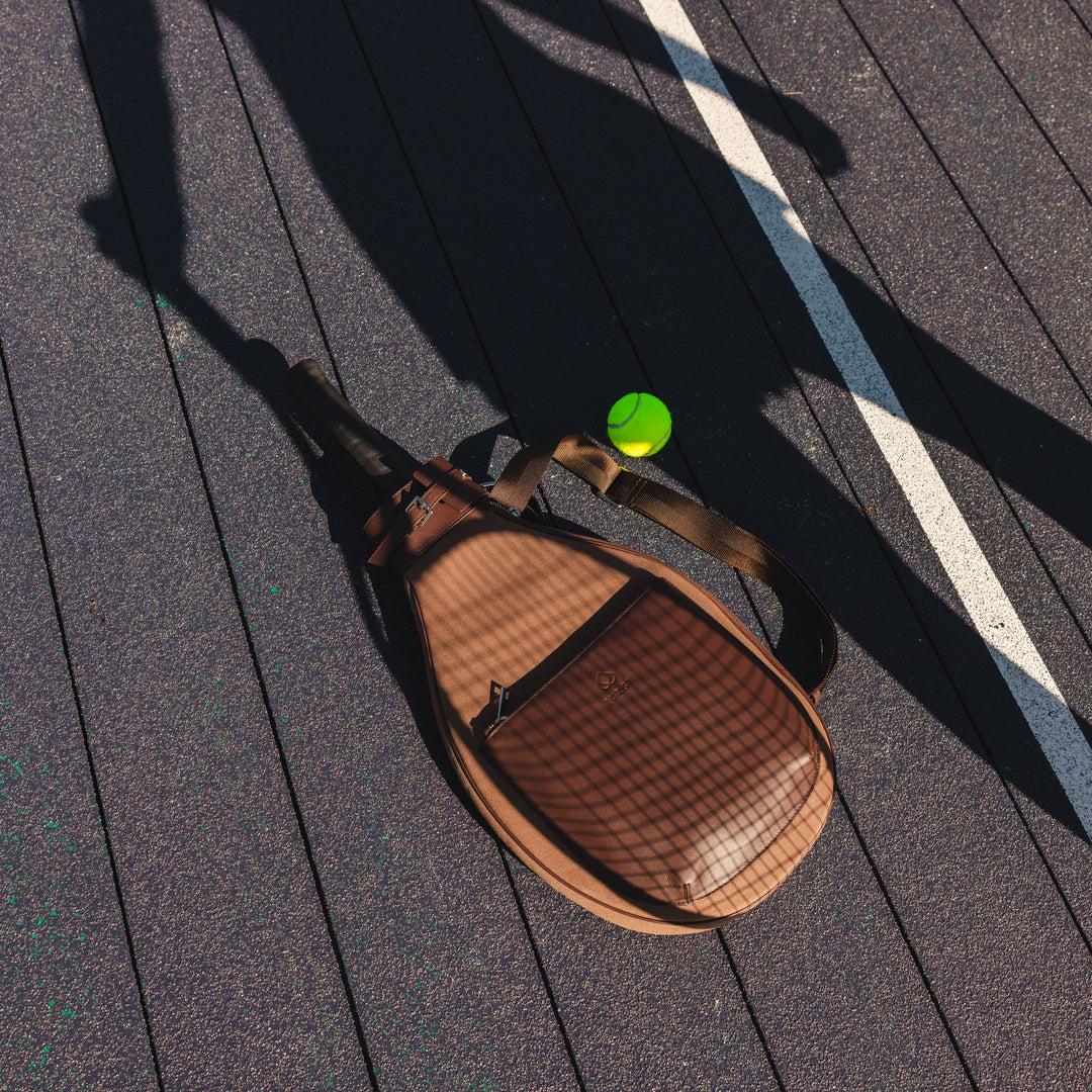 Brown tennis bag with a green ball on a wooden deck