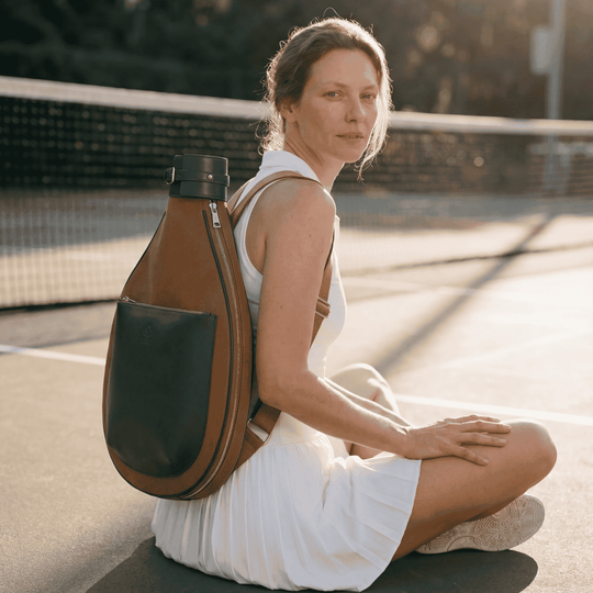 Woman sitting on a tennis court wearing a brown and green backpack