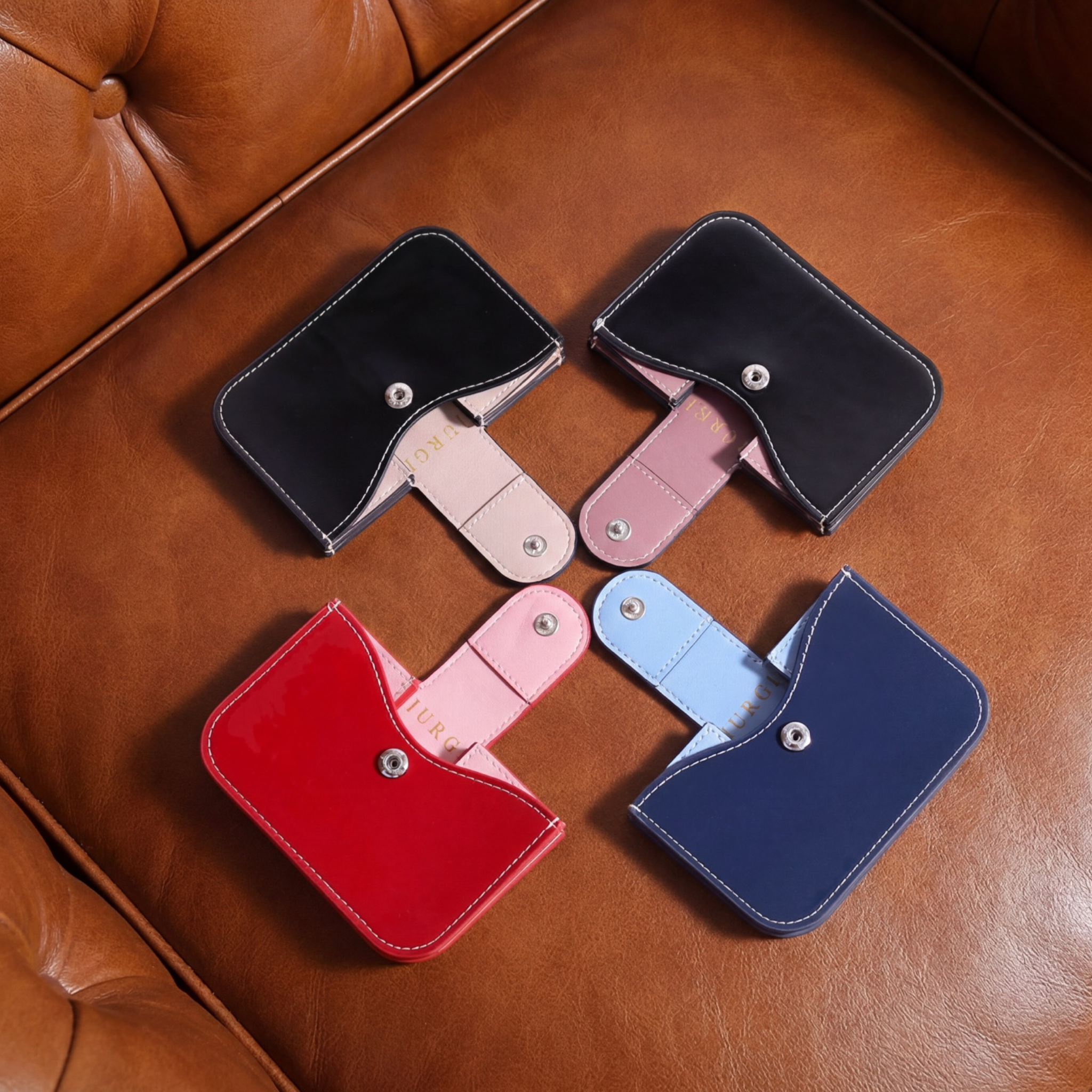 Four small patent leather accordion wallets in navy, black, and red with snap closures and contrasting interior panels.