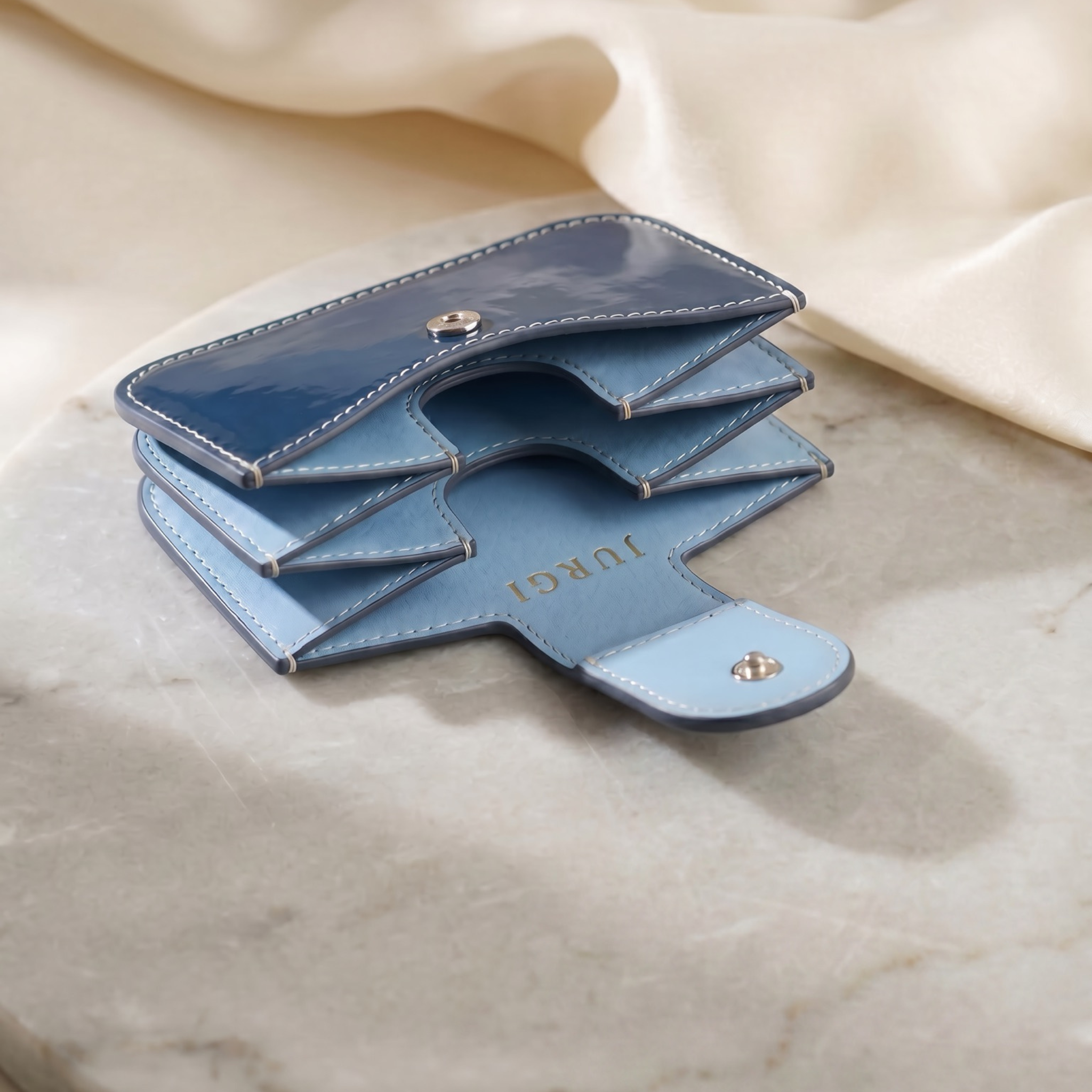 Navy patent leather accordion wallet with silver snap button and white contrast stitching, opened on marble surface.