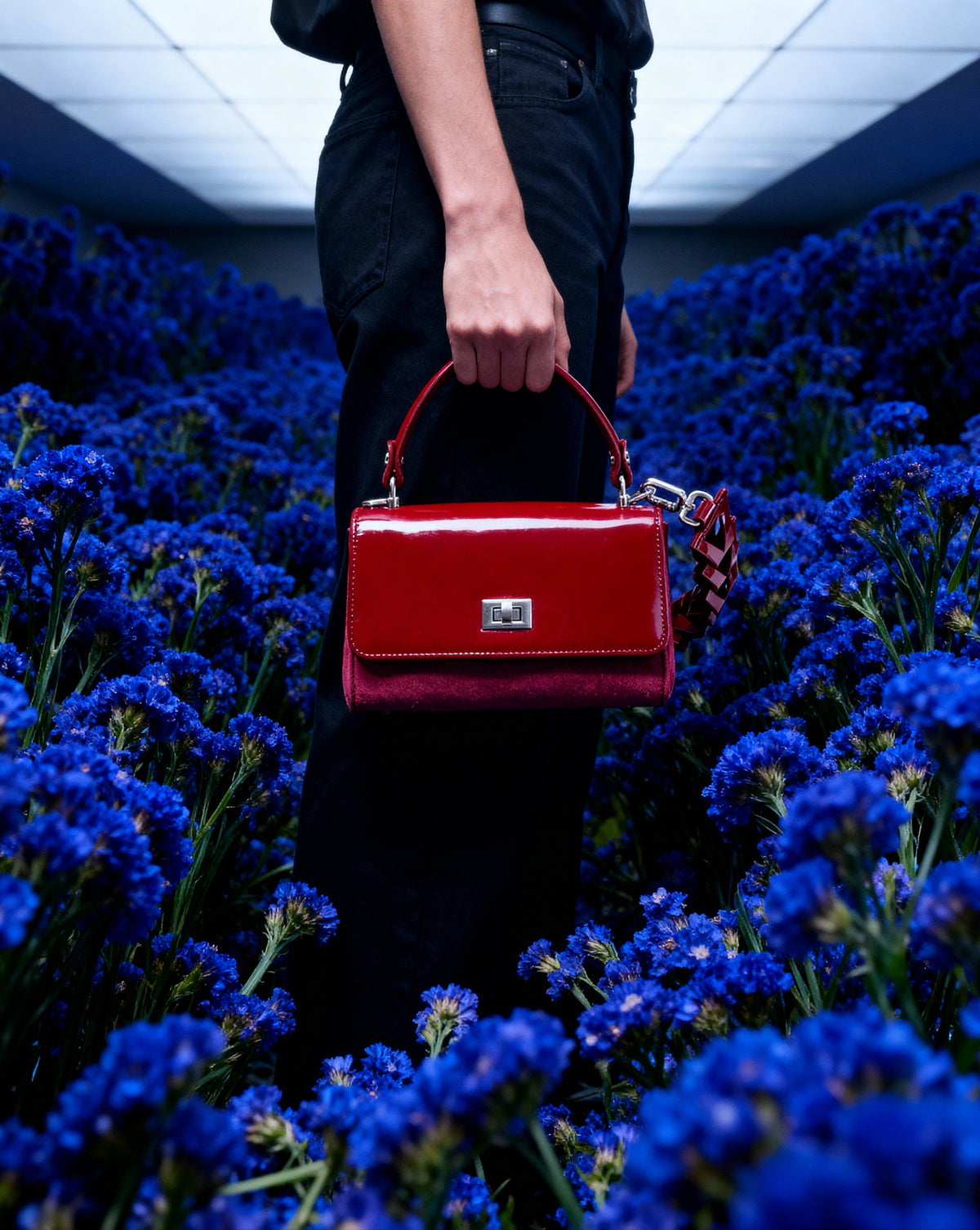 Red handbag held by a person standing among blue flowers