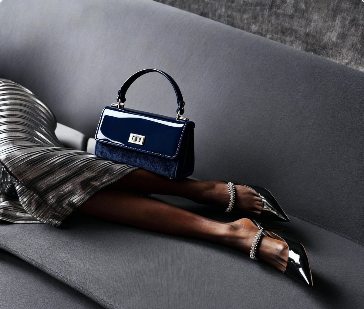 Person sitting on a gray couch with a navy handbag and striped dress.
