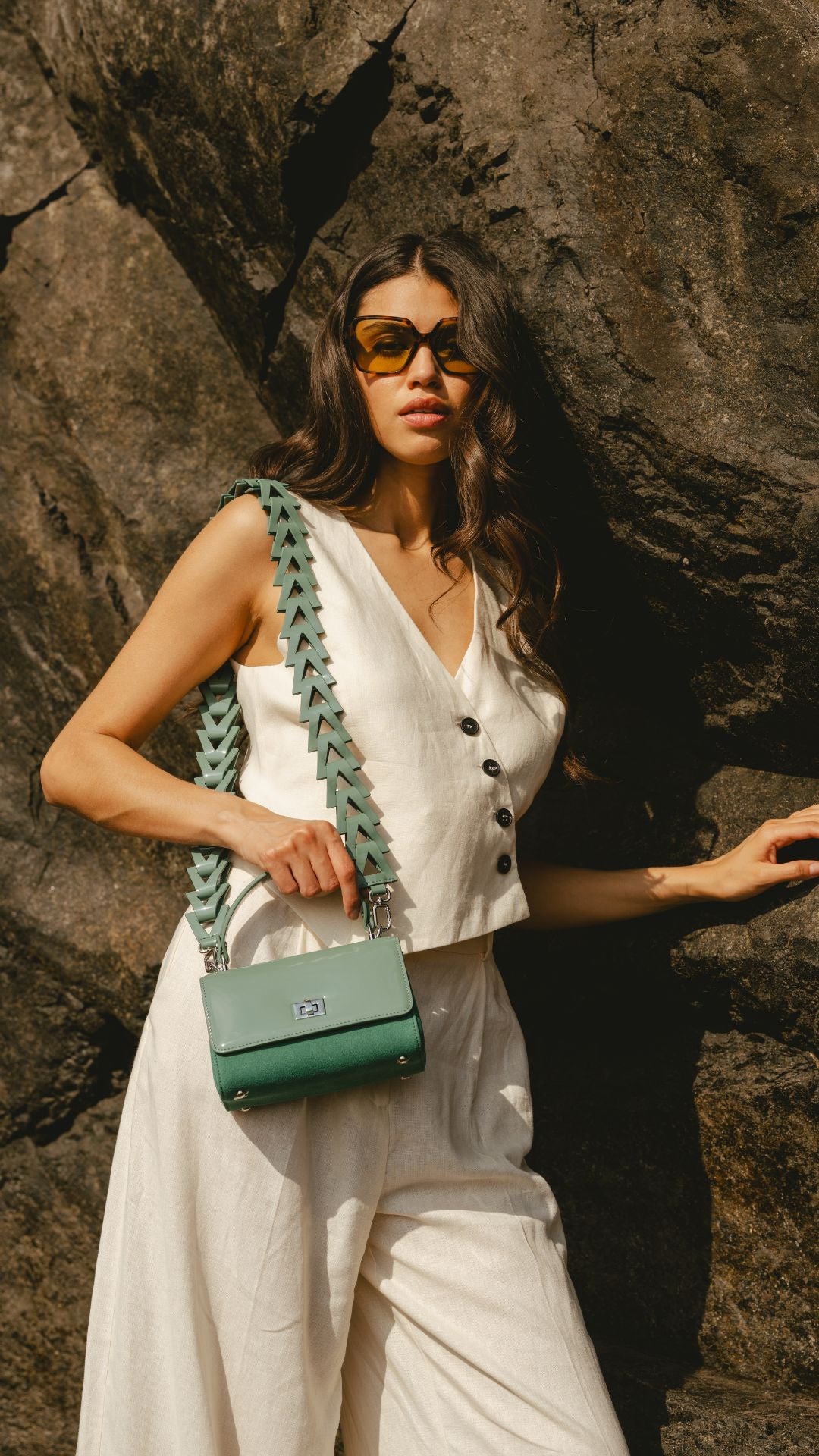 Woman  holding a green handbag against a rocky background