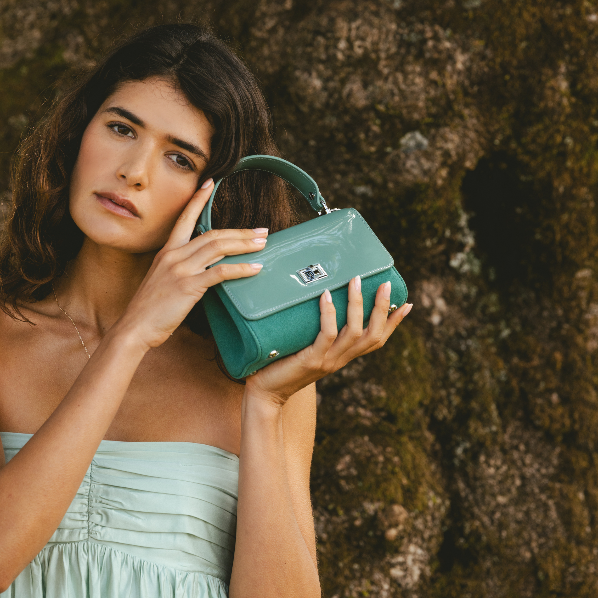 Woman holding a mint handbag against a textured wall in an event 