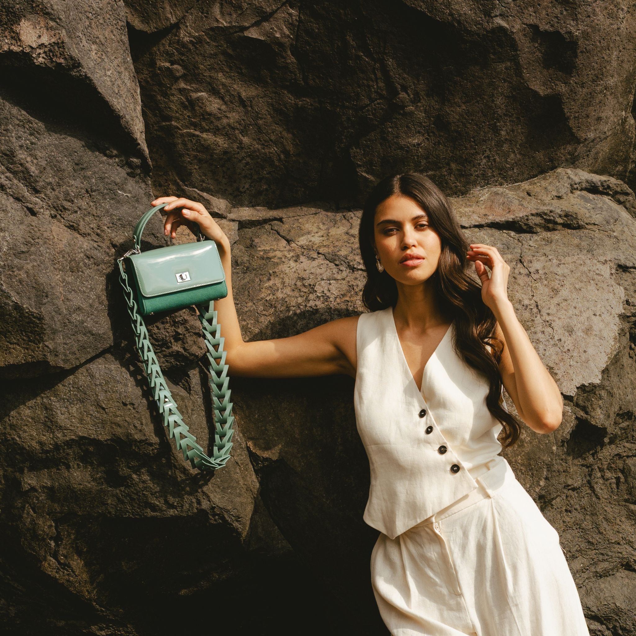 Woman holding a green handbag against a rocky background