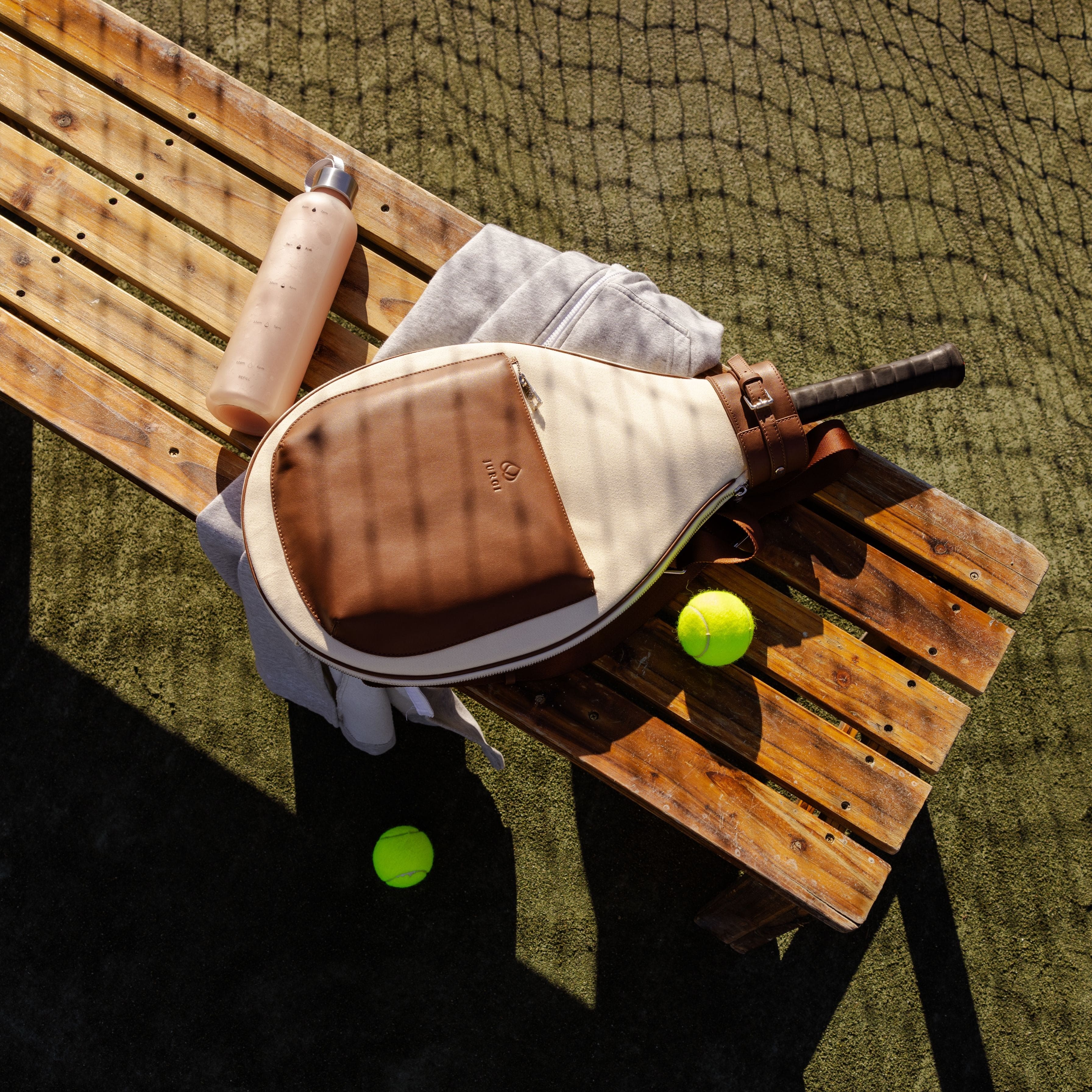 Tennis racket and ball on a wooden bench with a tennis court background 