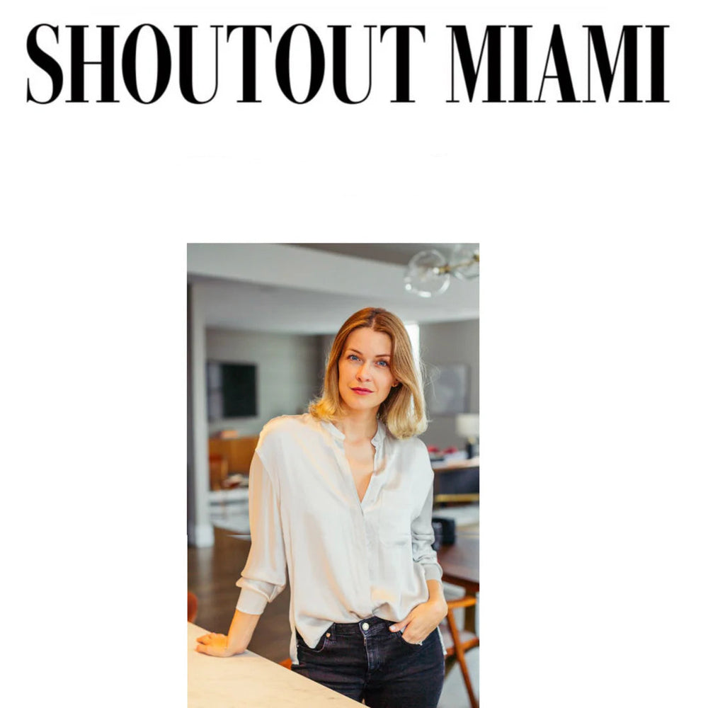 A woman with blonde hair wearing a white blouse and black pants stands in a modern kitchen, smiling slightly. The words SHOUTOUT MIAMI appear in large text above her.