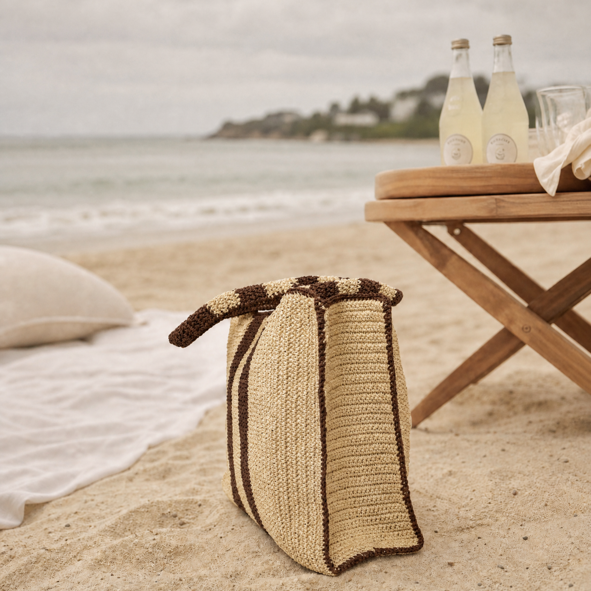 Woven brown and beige striped tote bag with a structured rectangular shape, shown on a sandy beach setting.