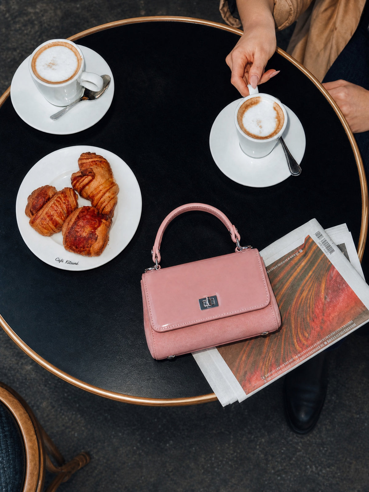 Pink handbag on a table with coffee, croissants, and a newspaper